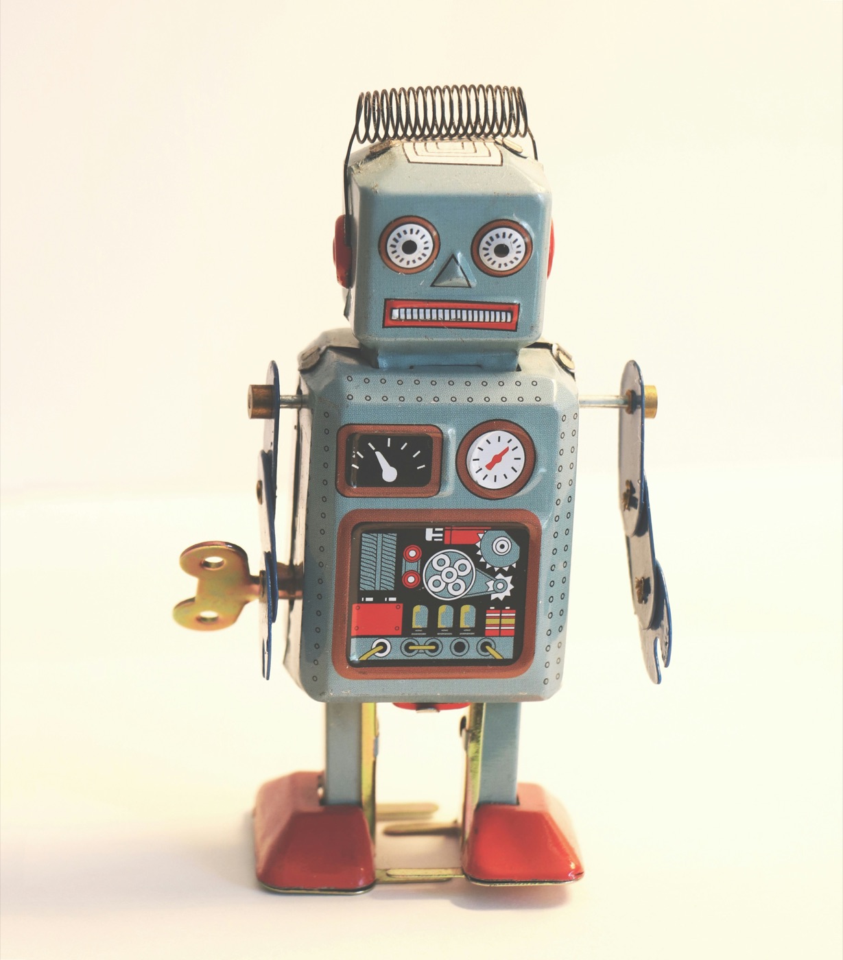 A vintage wind-up tin toy robot with a spring antenna and round dial eyes, photographed against a plain cream background.